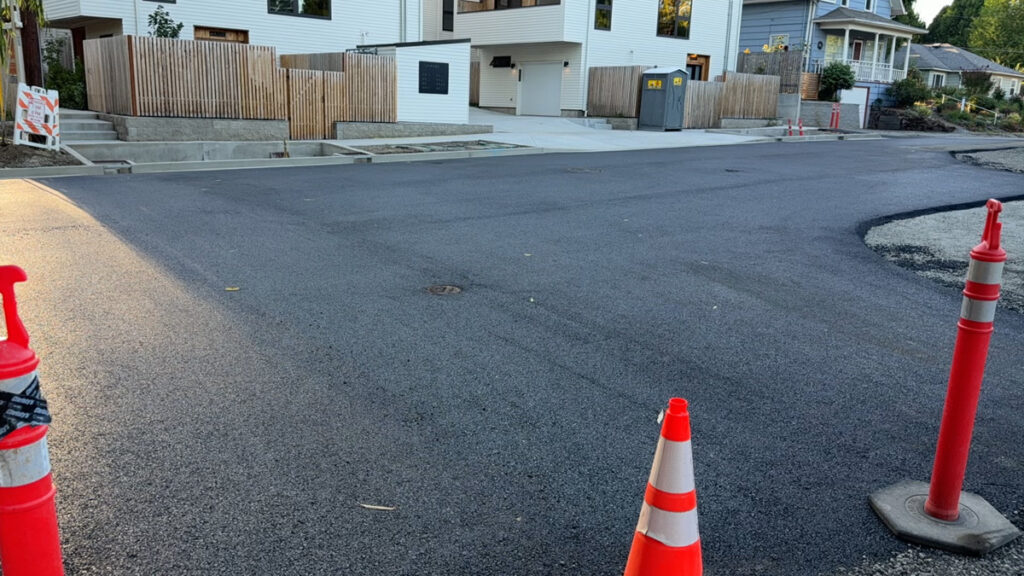 Newly paved asphalt roadway in a residential neighborhood with traffic cones set for safety during curing.